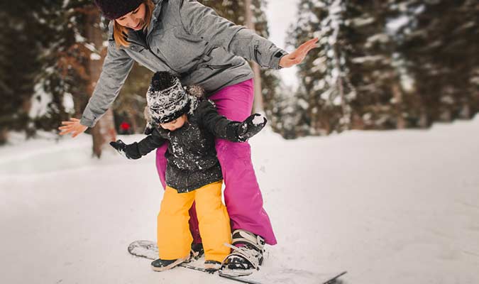 Mom helping child snowboard
